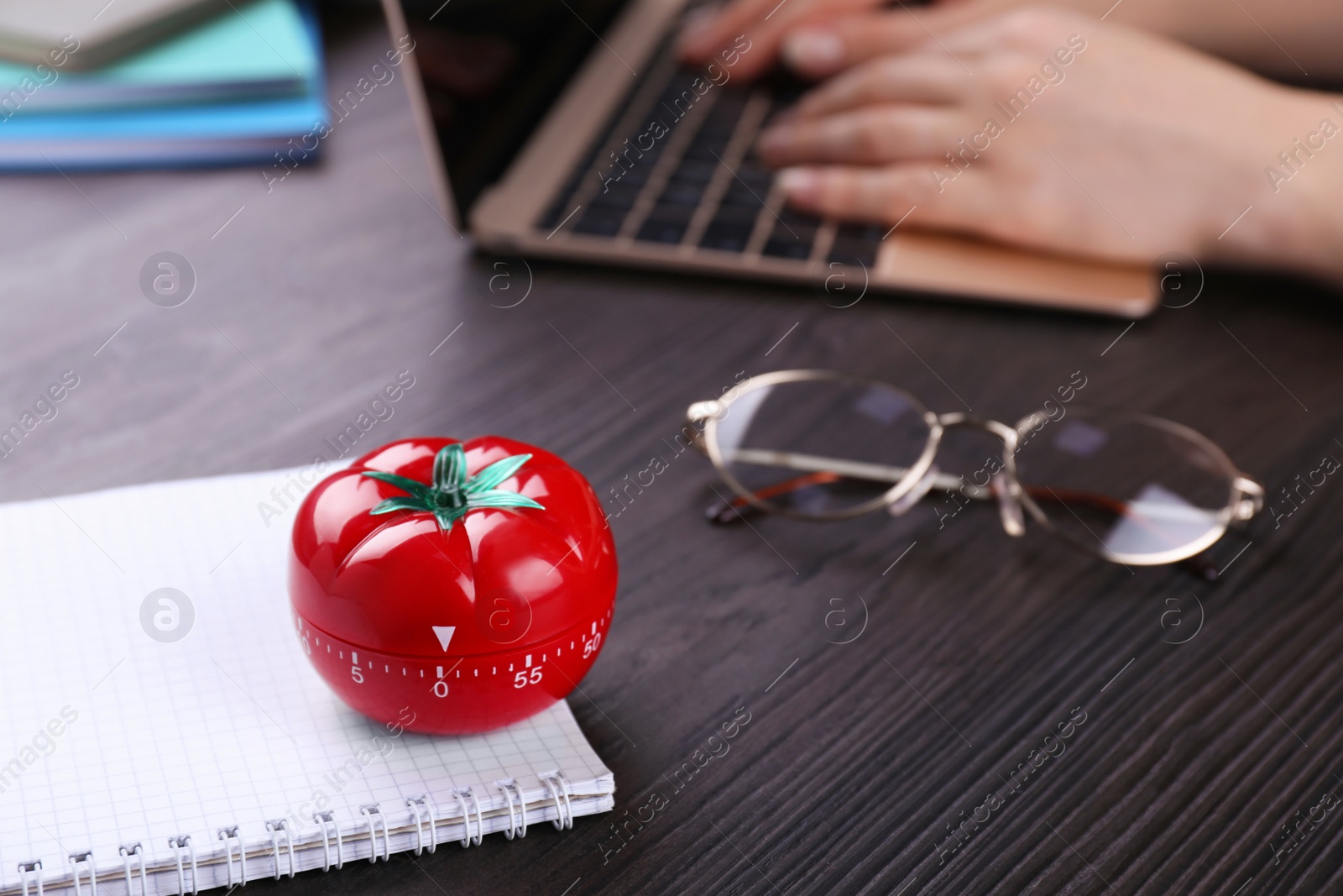 Photo of Woman working on laptop at wooden table, focus on kitchen timer in shape of tomato. Space for text