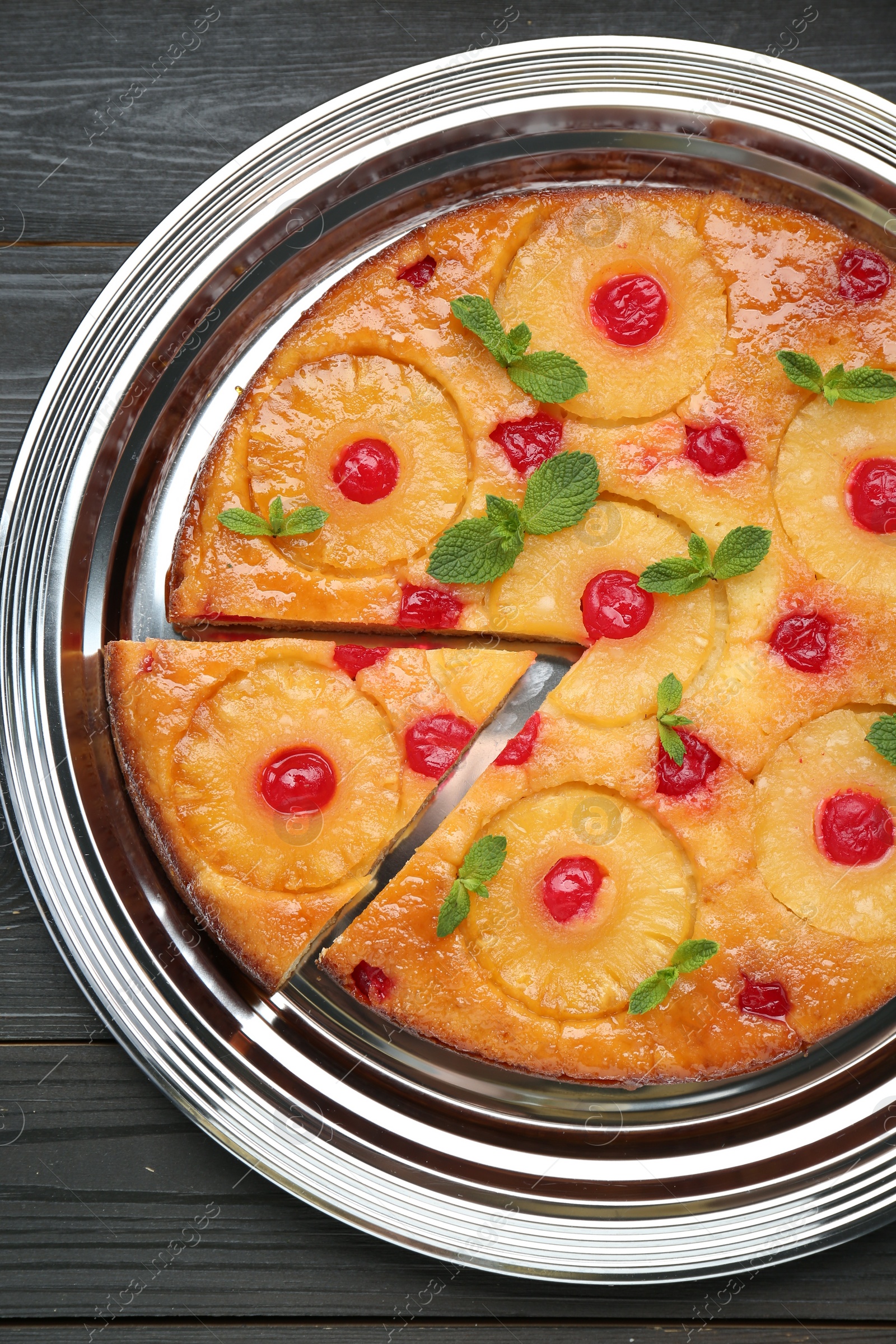 Photo of Delicious cut pineapple pie with cherry and mint on black wooden table, top view