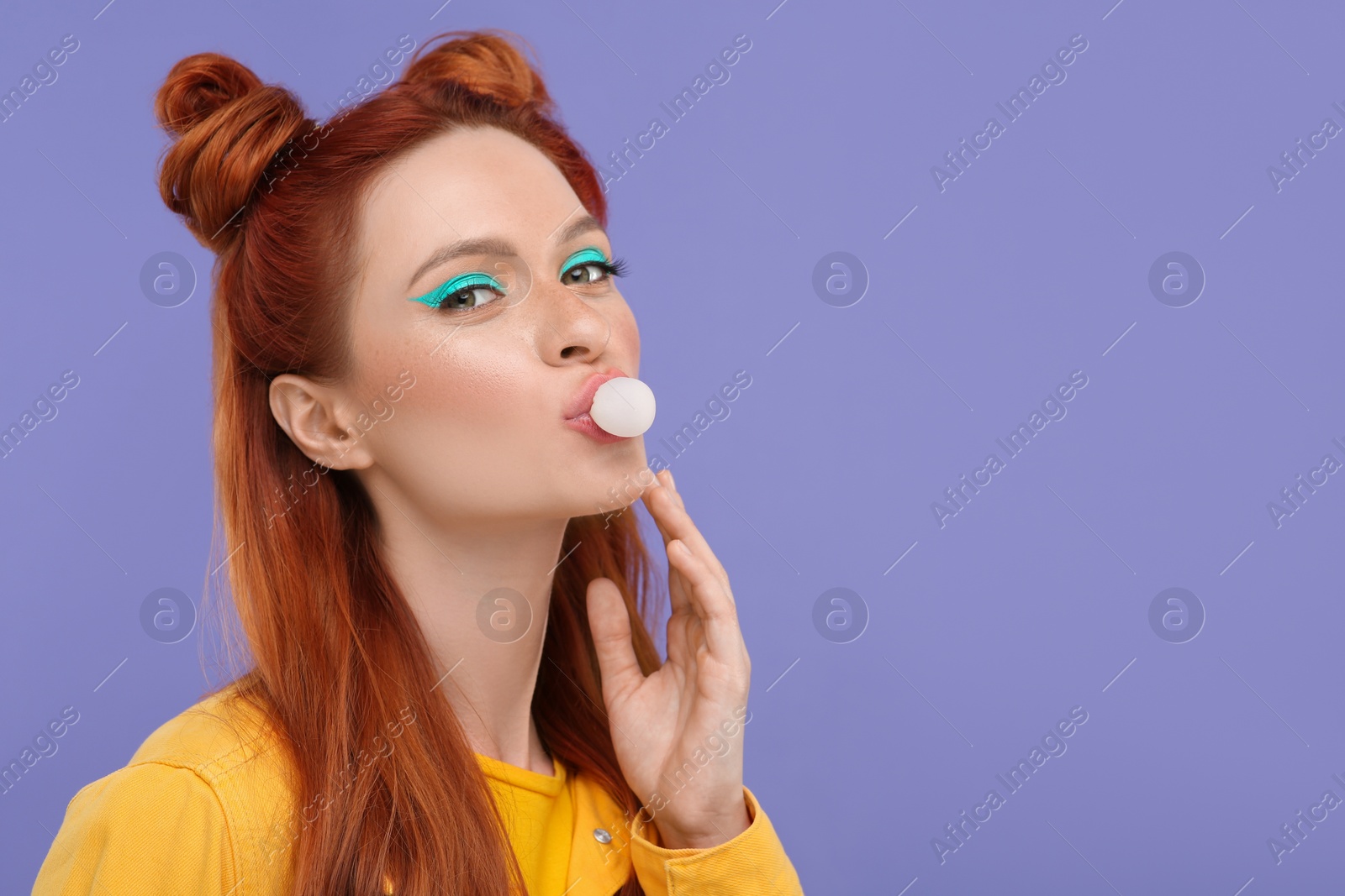 Photo of Portrait of beautiful woman with bright makeup blowing bubble gum on violet background. Space for text