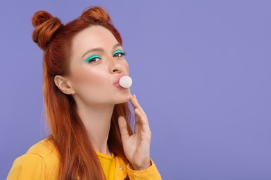 Photo of Portrait of beautiful woman with bright makeup blowing bubble gum on violet background. Space for text