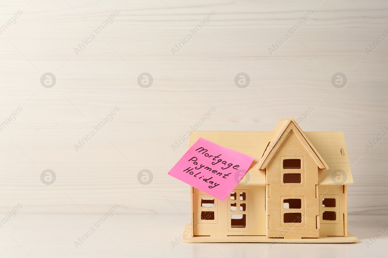 Photo of Paper note with words Mortgage Payment Holiday and house model on white wooden table, space for text