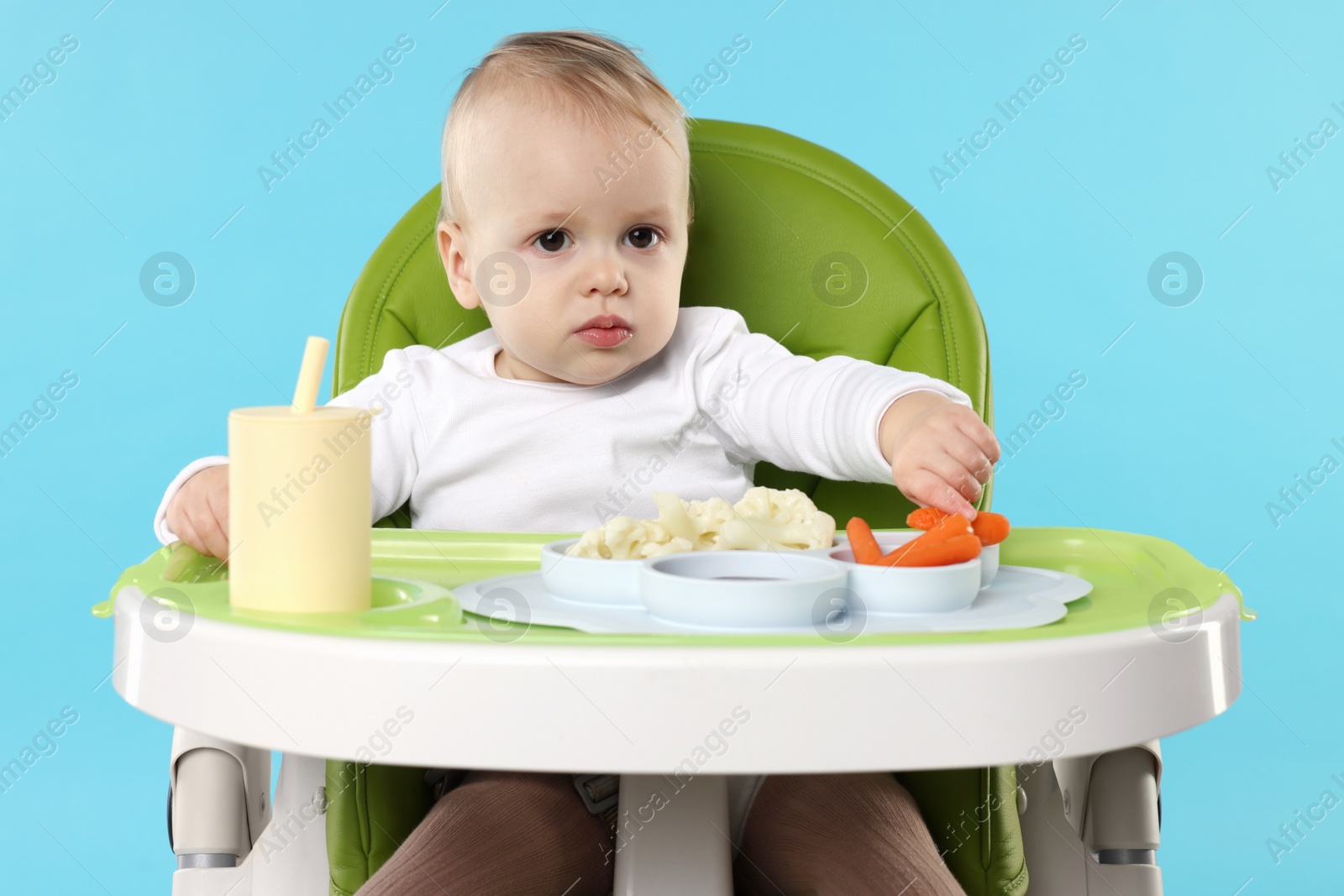 Photo of Cute little baby with healthy food in high chair on light blue background