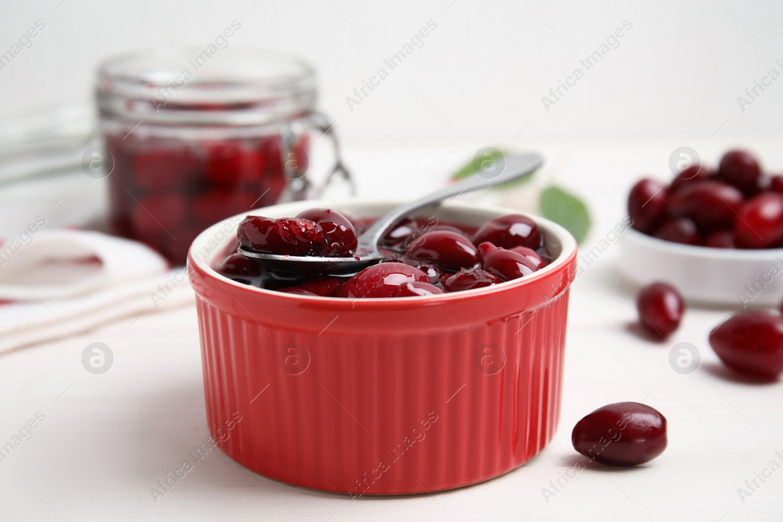 Photo of Delicious dogwood jam with berries and spoon on white wooden table, closeup