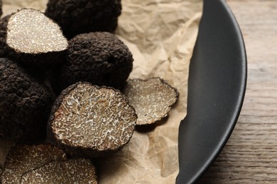 Photo of Whole and cut black truffles with parchment on plate, closeup