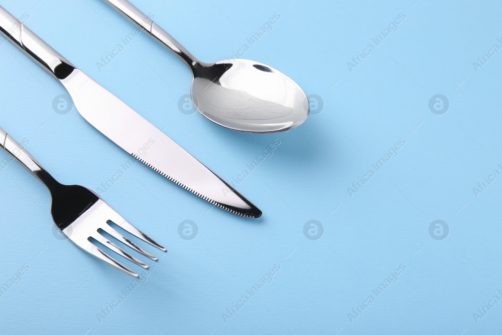 Photo of Stylish silver cutlery set on light blue background, closeup. Space for text