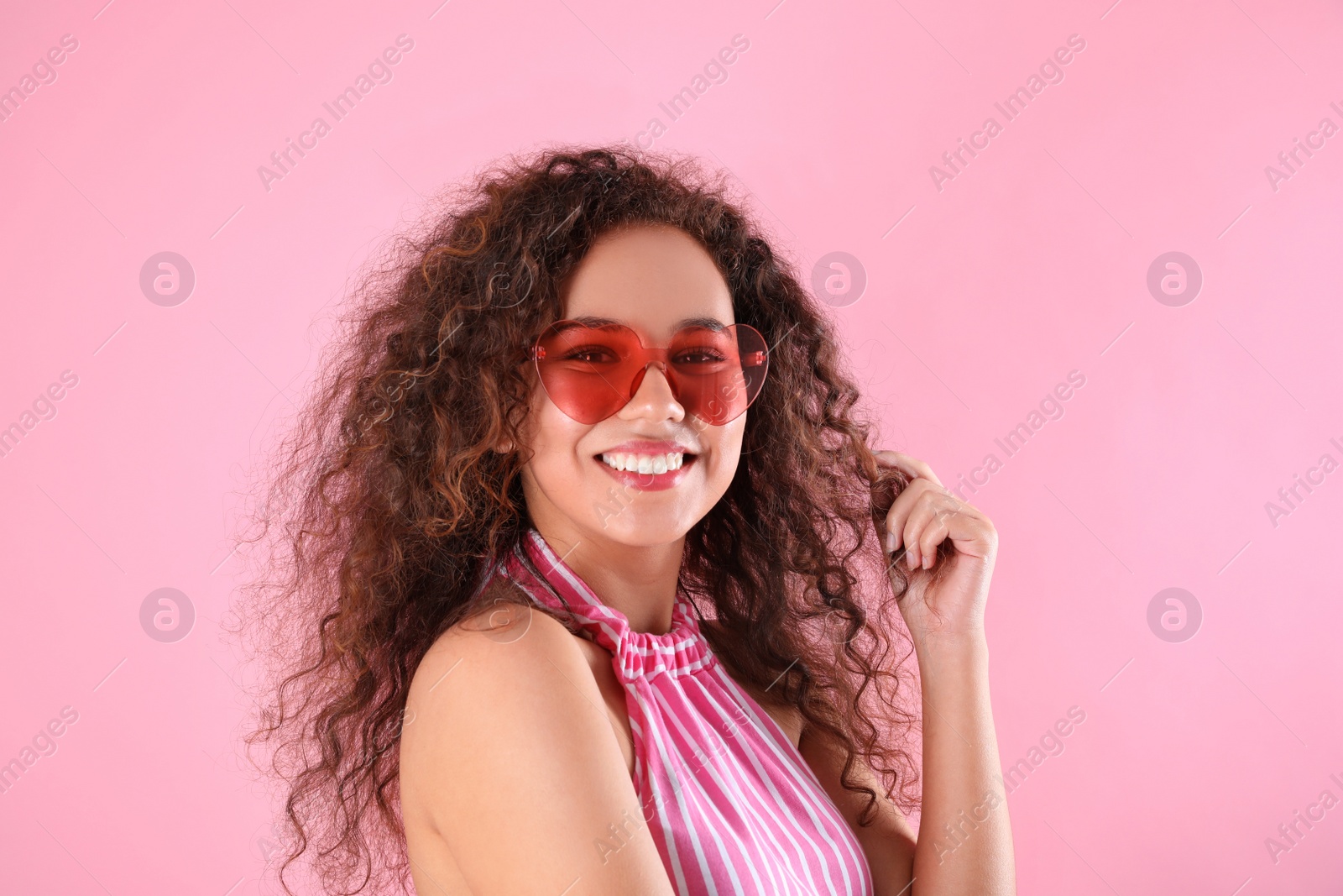 Photo of Young beautiful African-American woman wearing heart shaped glasses on pink background