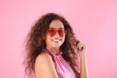 Young beautiful African-American woman wearing heart shaped glasses on pink background