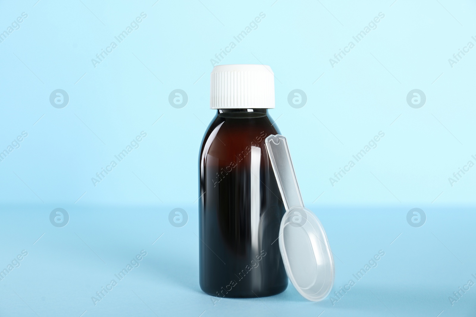 Photo of Bottle of cough syrup and dosing spoon on light blue background