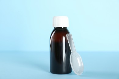 Photo of Bottle of cough syrup and dosing spoon on light blue background