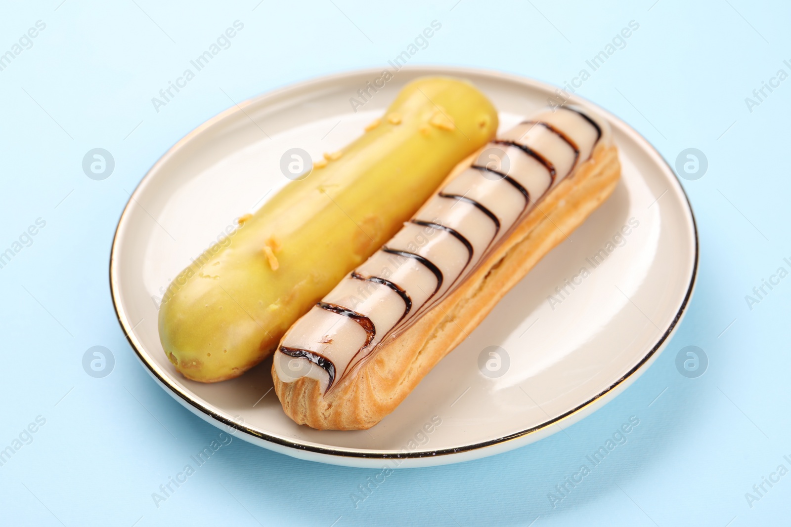 Photo of Delicious eclairs covered with glaze on light blue background