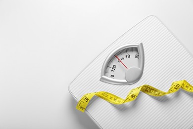 Photo of Scales and measuring tape on white background, top view. Space for text