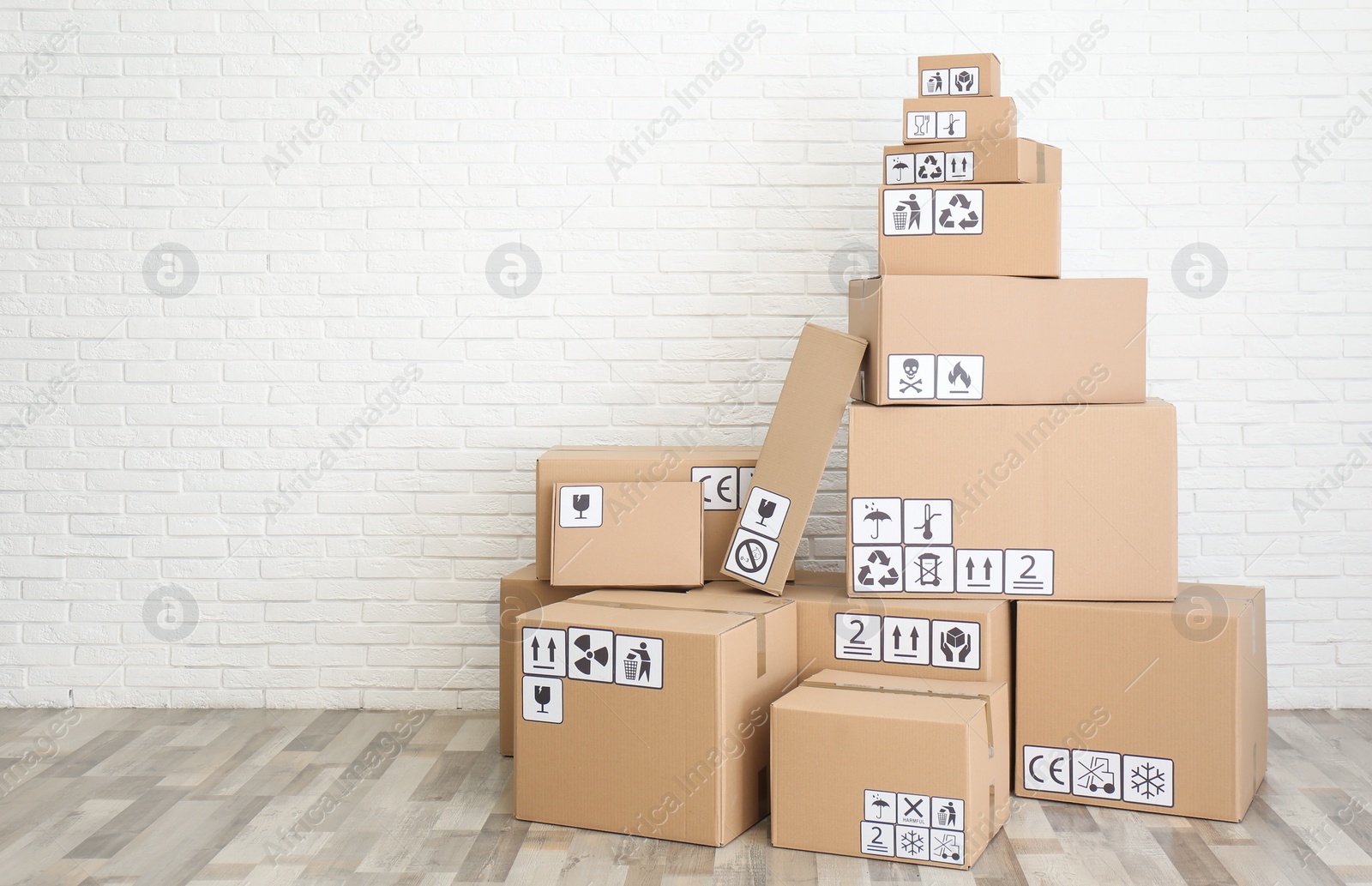 Photo of Cardboard boxes with different packaging symbols on floor near white brick wall, space for text. Parcel delivery