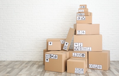 Photo of Cardboard boxes with different packaging symbols on floor near white brick wall, space for text. Parcel delivery