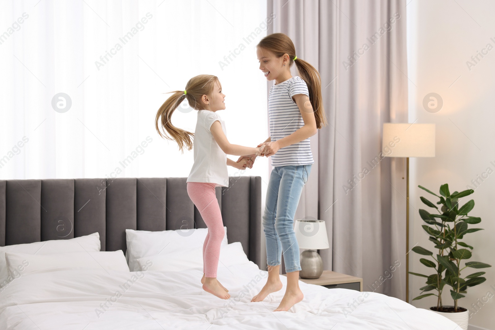 Photo of Cute little sisters having fun together on bed at home