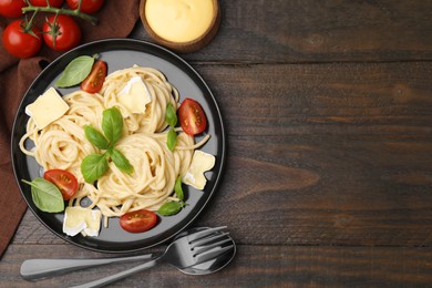 Delicious pasta with brie cheese, tomatoes and basil served on wooden table, flat lay. Space for text
