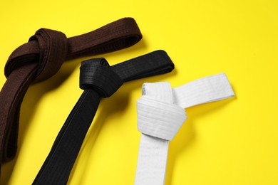 Photo of Colorful karate belts on yellow background, flat lay