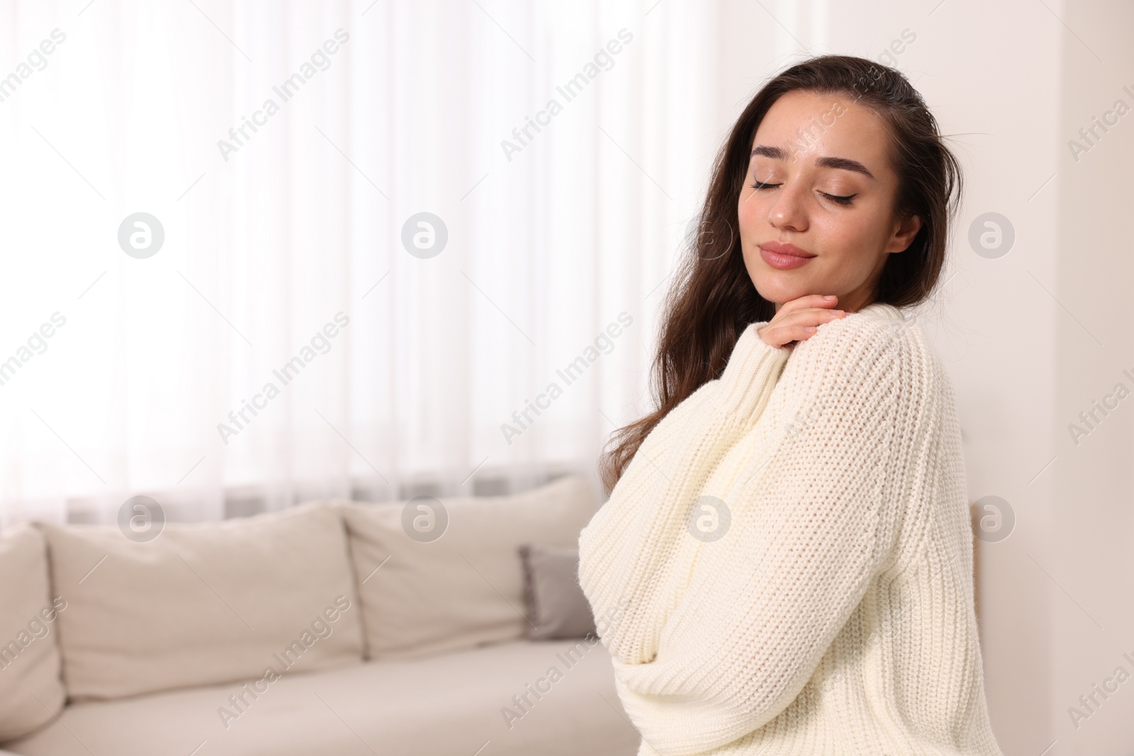 Photo of Beautiful young woman in stylish warm sweater at home, space for text