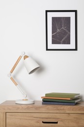 Desk lamp and books on wooden chest of drawers indoors