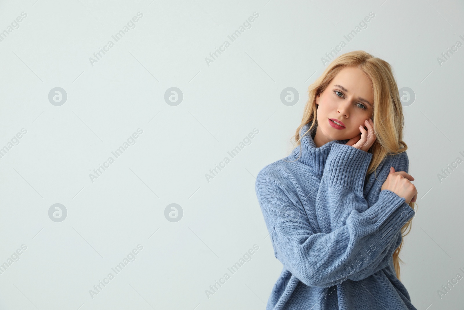 Photo of Beautiful young woman wearing warm blue sweater on light background. Space for text