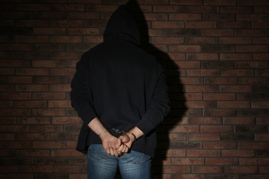 Male criminal in handcuffs near brick wall