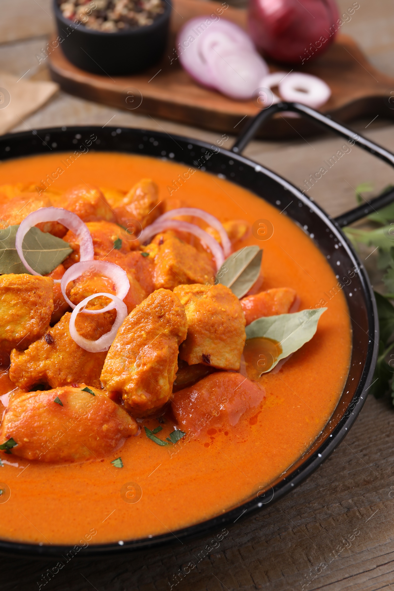 Photo of Delicious chicken curry in pan on wooden table, closeup