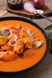 Photo of Delicious chicken curry in pan on wooden table, closeup