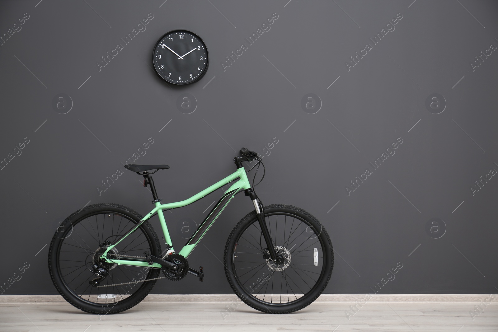 Photo of Modern green bicycle near grey wall indoors. Space for text