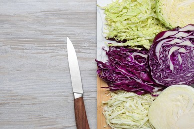 Photo of Different types of cut cabbage and knife on white wooden table, flat lay. Space for text