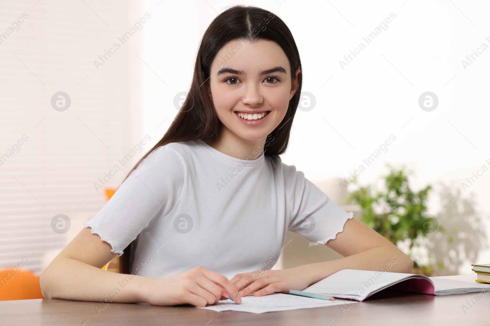 Photo of Teenage girl erasing mistake in her notebook at wooden desk indoors