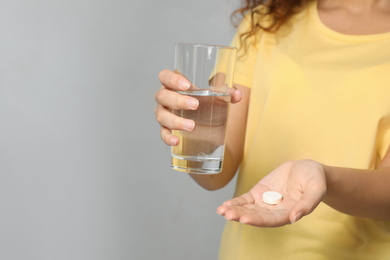 Photo of African-American woman with glass of water and vitamin pill on light grey background, closeup. Space for text