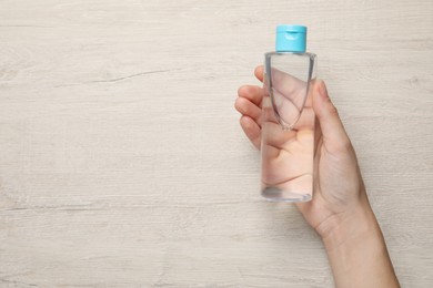 Photo of Woman holding micellar water in bottle against wooden background, top view. Space for text