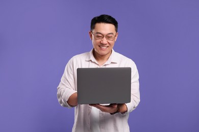 Happy man with laptop on lilac background