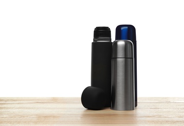 Stylish thermo bottles on wooden table against white background