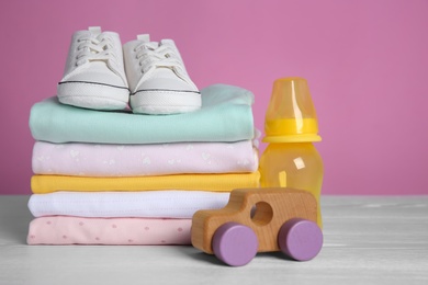 Photo of Children's shoes, stack of clothes and toy on white wooden table