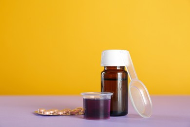 Photo of Bottle of cough syrup, measuring cup, dosing spoon and pills on color background. Space for text