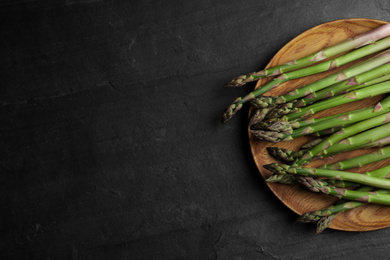 Photo of Fresh raw asparagus on black table, top view. Space for text