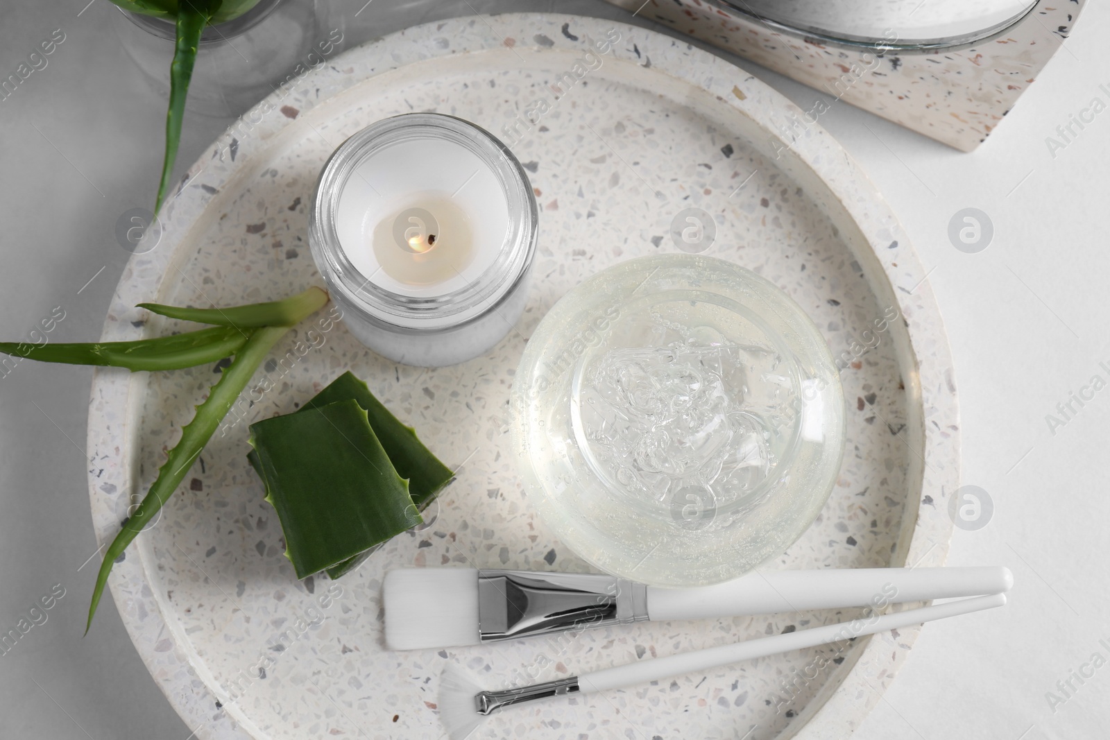 Photo of Jar of natural gel, burning candle, makeup brushes and fresh aloe leaves on white table, top view