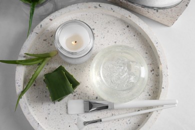 Photo of Jar of natural gel, burning candle, makeup brushes and fresh aloe leaves on white table, top view