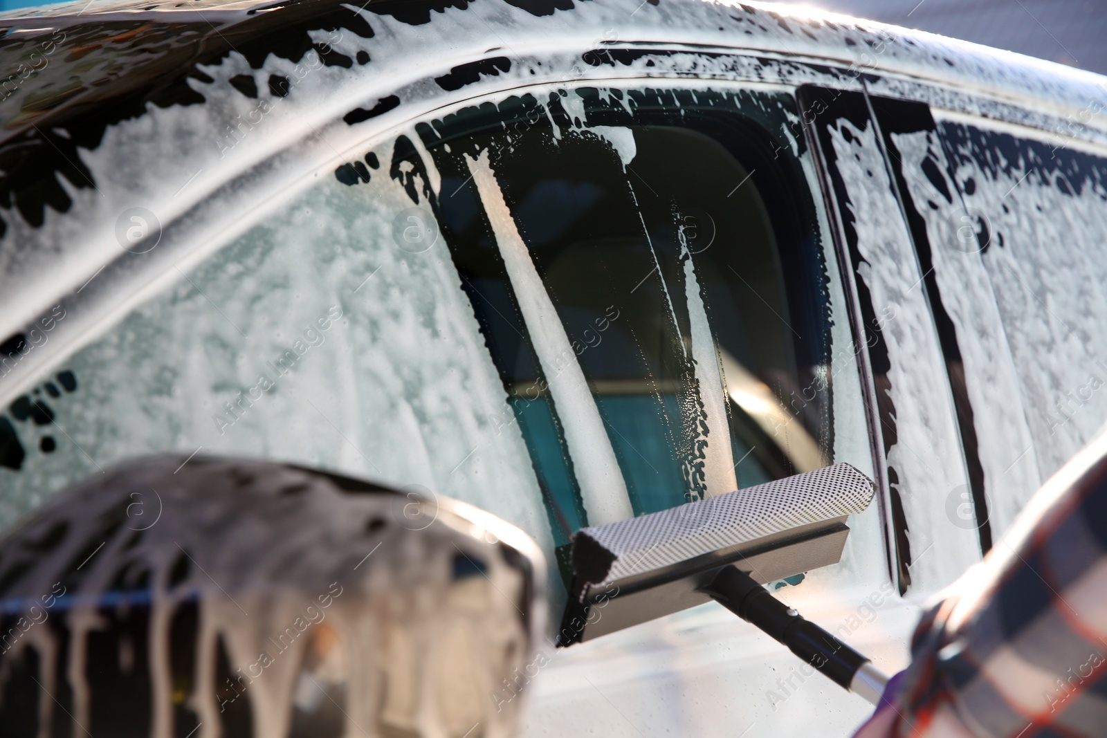 Photo of Worker cleaning automobile window with squeegee at car wash, closeup