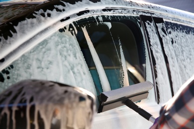 Photo of Worker cleaning automobile window with squeegee at car wash, closeup