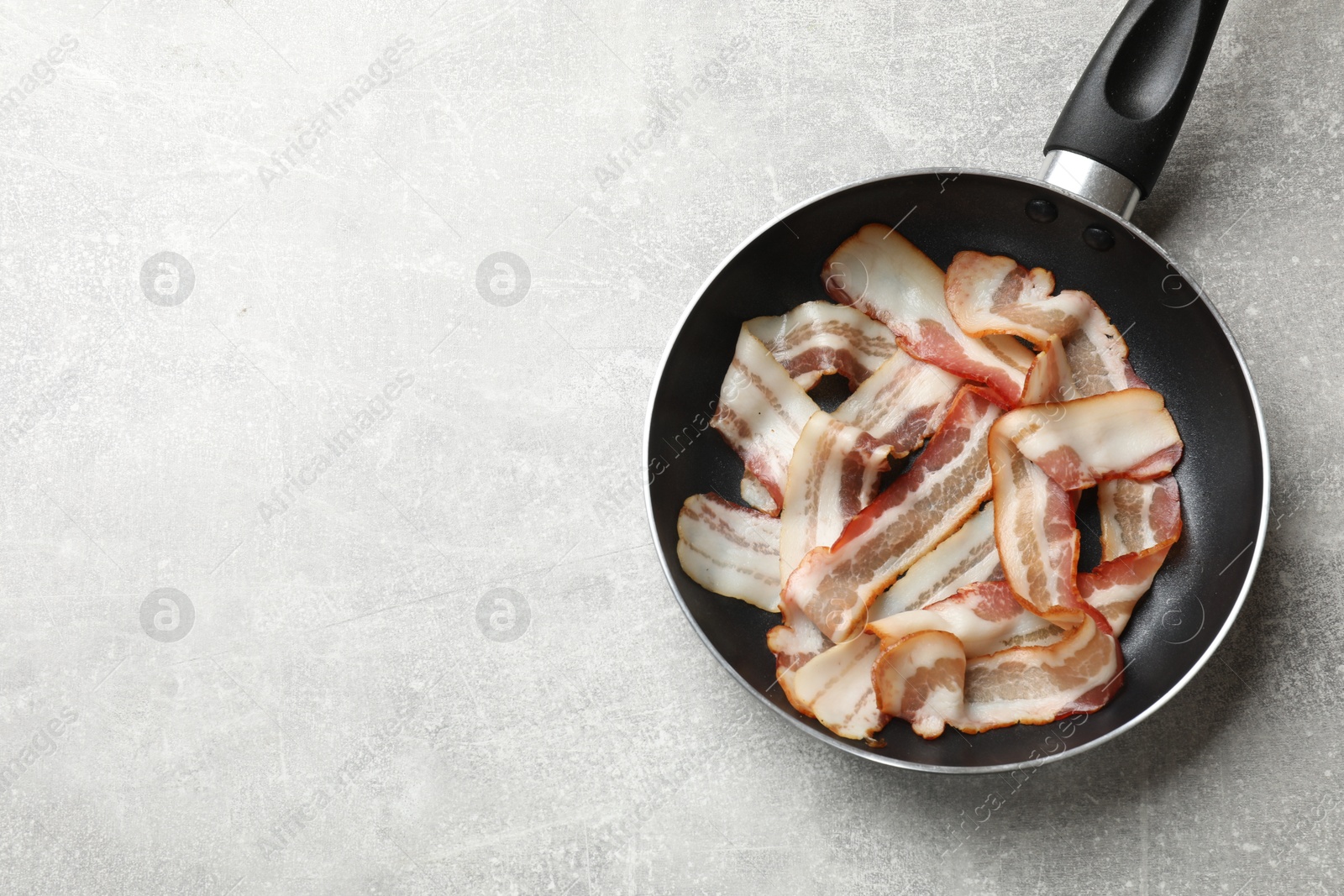 Photo of Delicious bacon slices in frying pan on light grey table, top view. Space for text