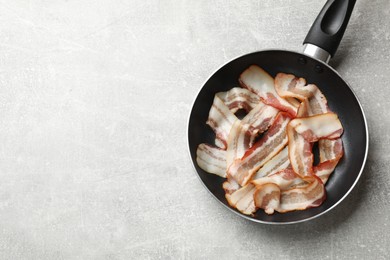 Delicious bacon slices in frying pan on light grey table, top view. Space for text