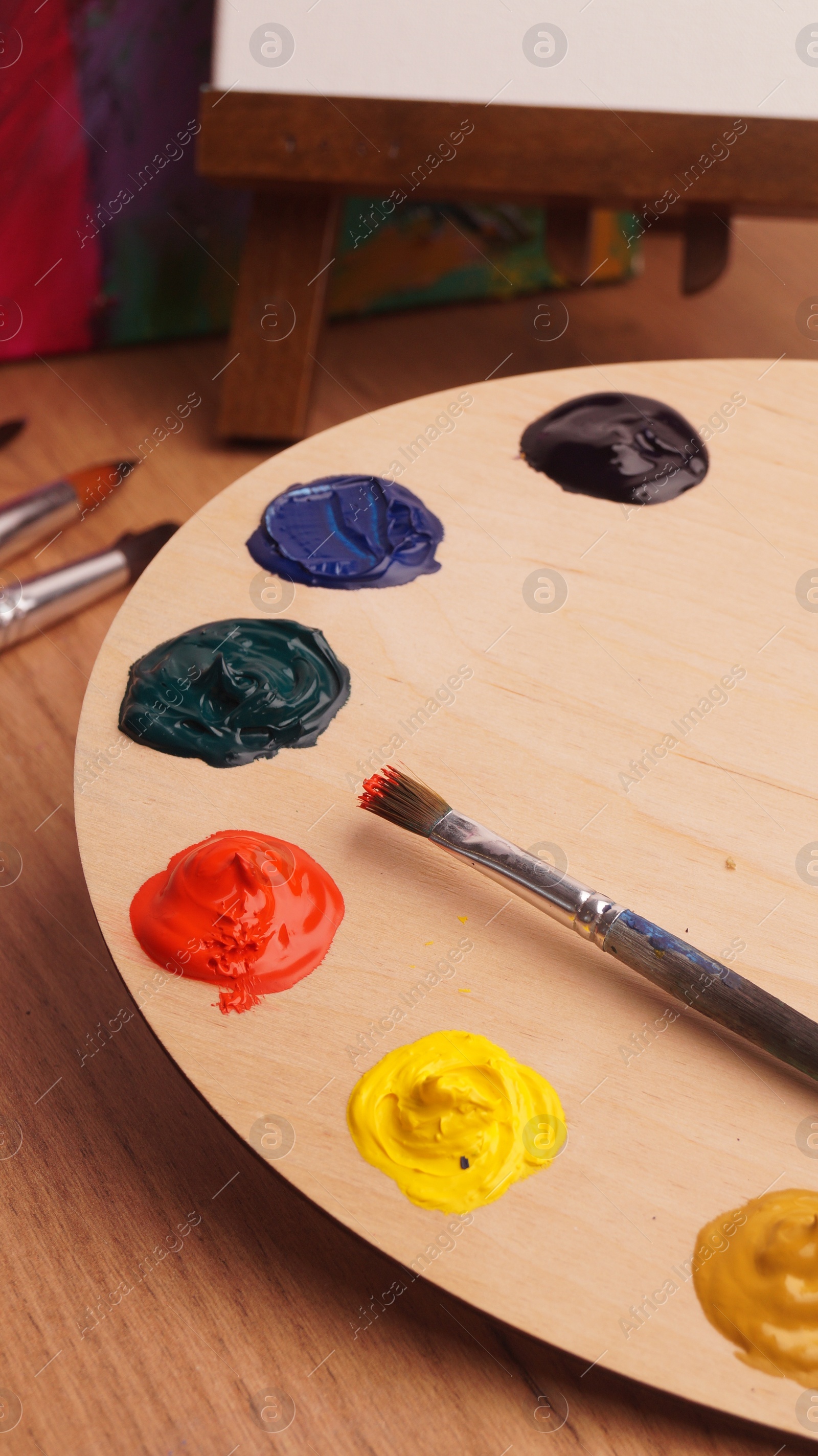 Photo of Artist's palette with samples of colorful paints and brush on wooden table