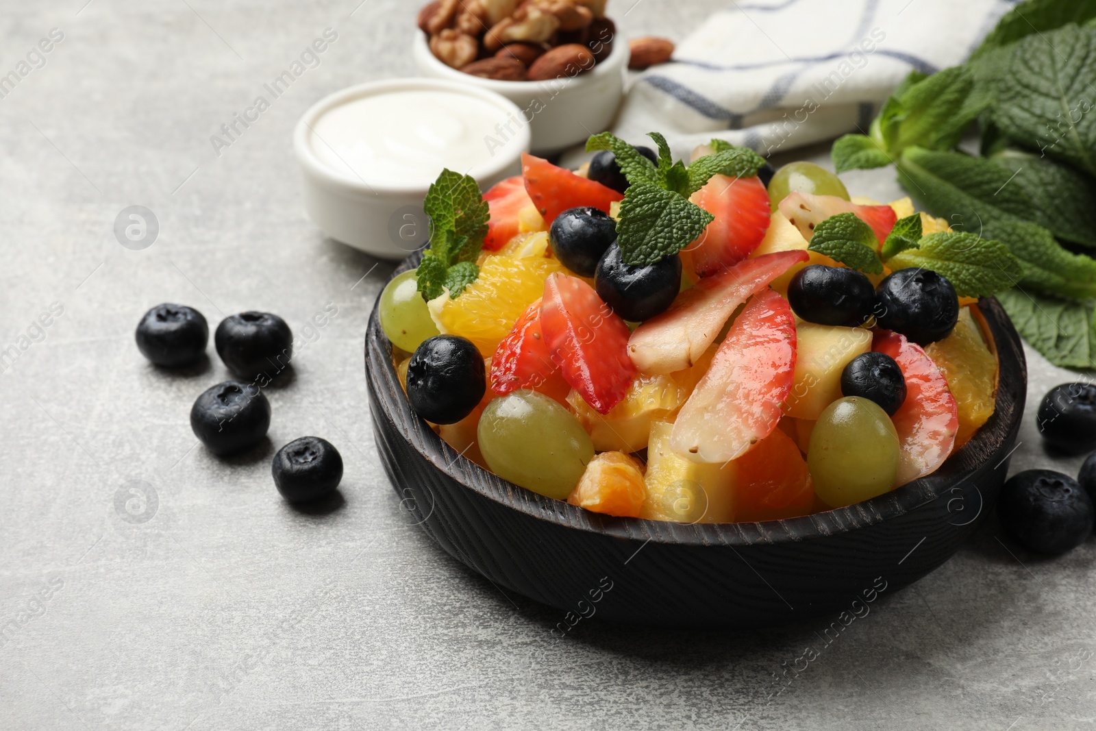 Photo of Delicious fruit salad in bowl, berries, nuts and fresh mint on grey table