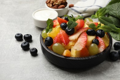 Photo of Delicious fruit salad in bowl, berries, nuts and fresh mint on grey table
