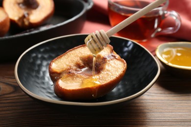 Photo of Pouring honey onto tasty baked quince in bowl at wooden table, closeup