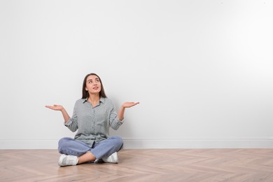 Young woman sitting on floor near white wall indoors. Space for text
