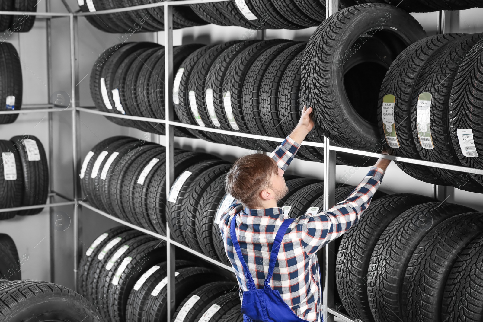 Photo of Young male mechanic with car tires in automobile service center