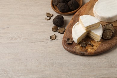 Photo of Delicious cheese and fresh black truffles on white wooden table. Space for text