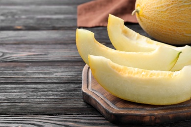 Photo of Pieces of delicious honeydew melon on black wooden table. Space for text